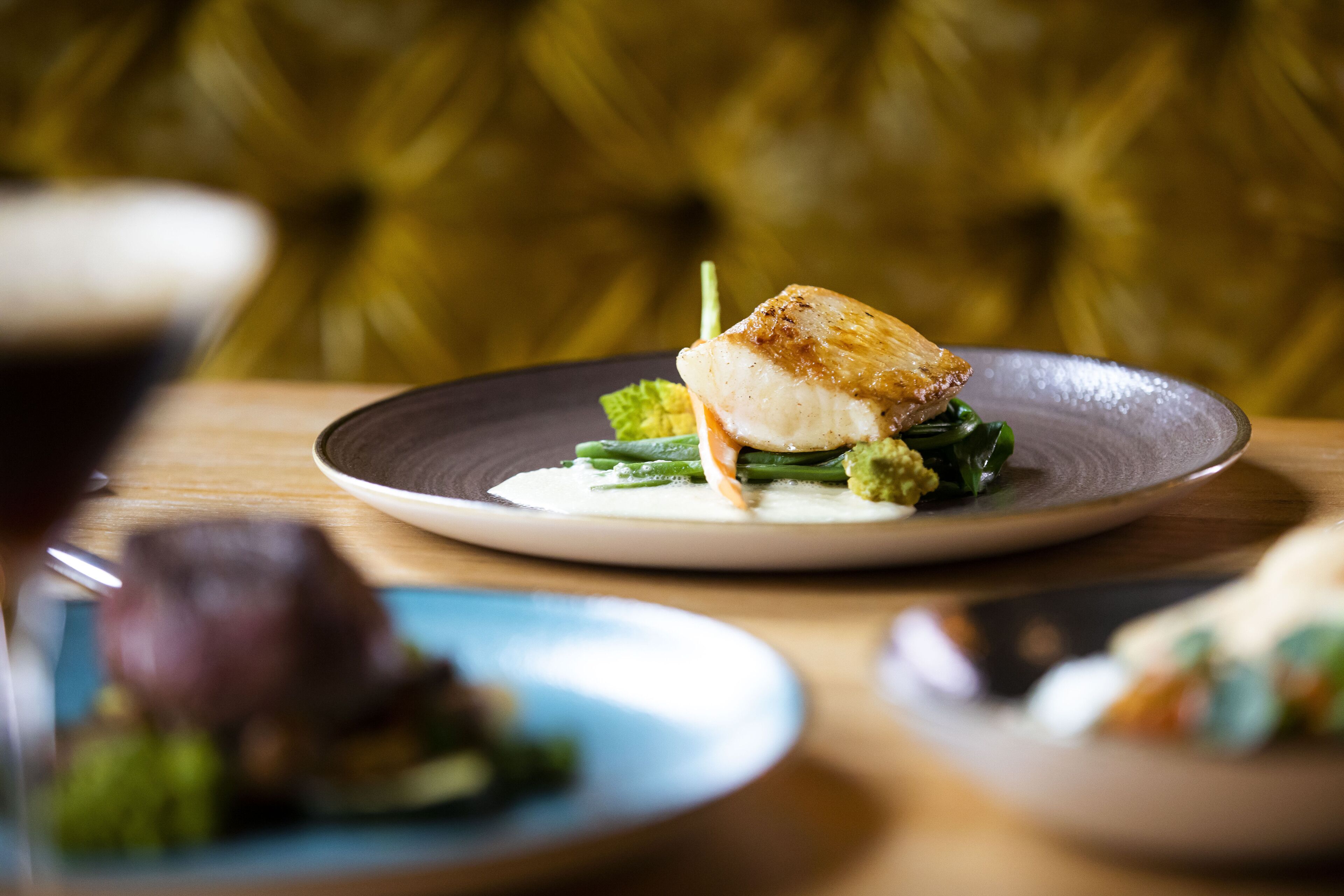 A plate of food with a piece of fish on a bed of greens, served on a dark plate.