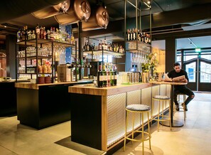 Zona de bar con un cantinero, estantes llenos de botellas de licor, vasos y una máquina de café.