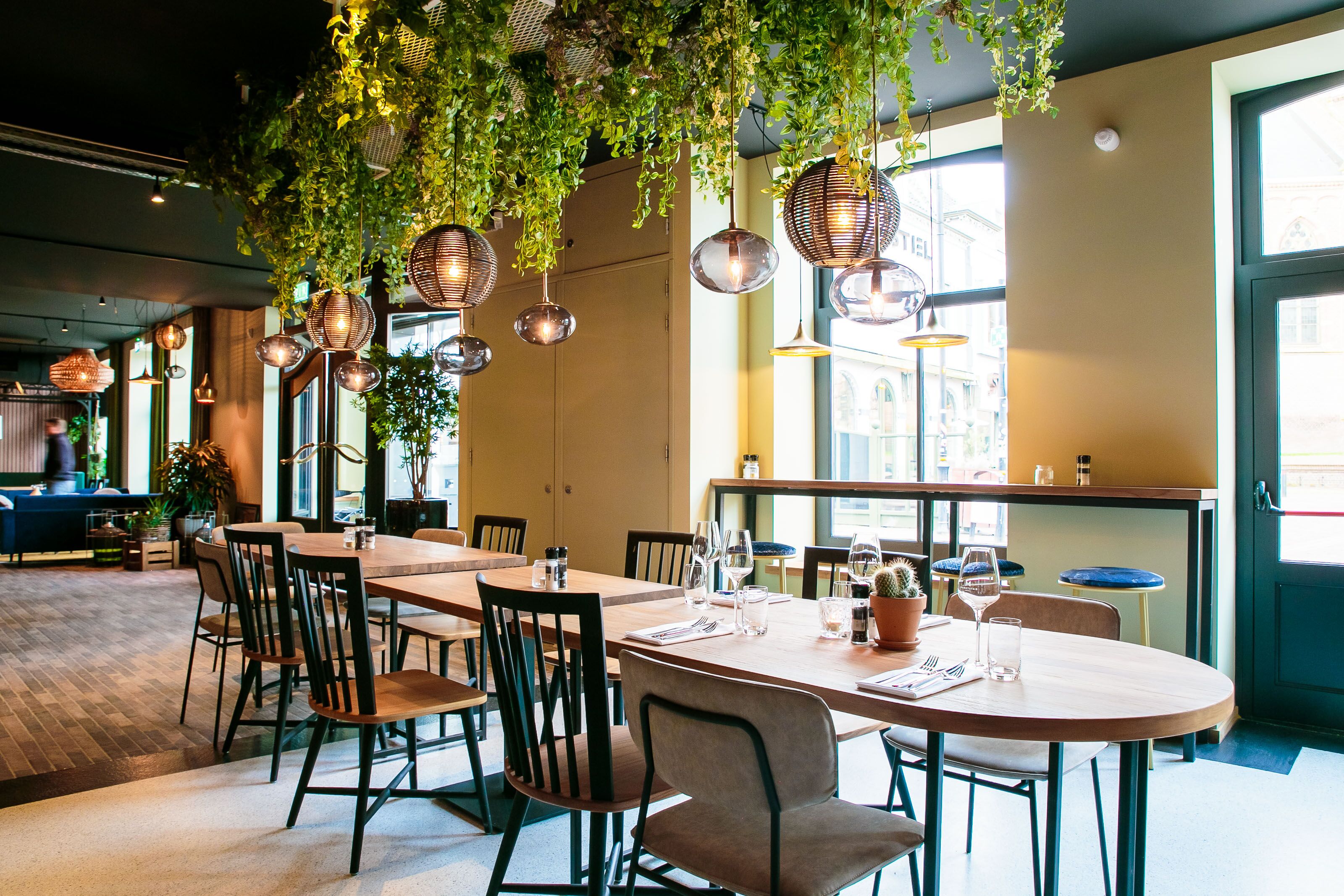 Un restaurant avec des tables rondes, des chaises, des plantes suspendues et des luminaires suspendus.