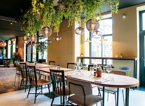 Un espace repas avec des tables, des chaises, des plantes suspendues et des luminaires suspendus.