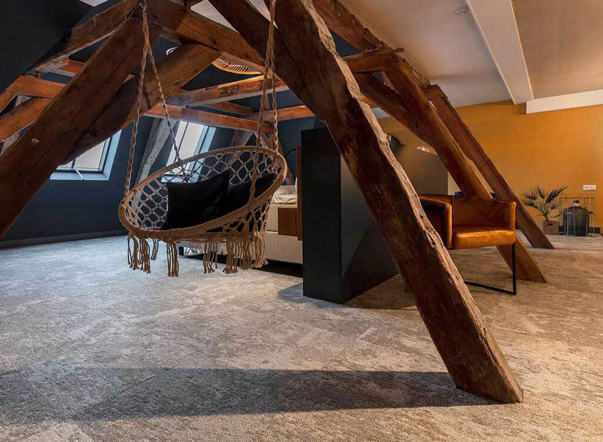 A room with a hanging swing chair, wooden beams, and a view of the sky through a window.
