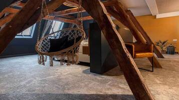 A room with a hanging swing chair, wooden beams, and a view of the sky through a window.