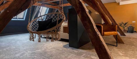 A room with a hanging swing chair, wooden beams, and a view of the sky through a window.