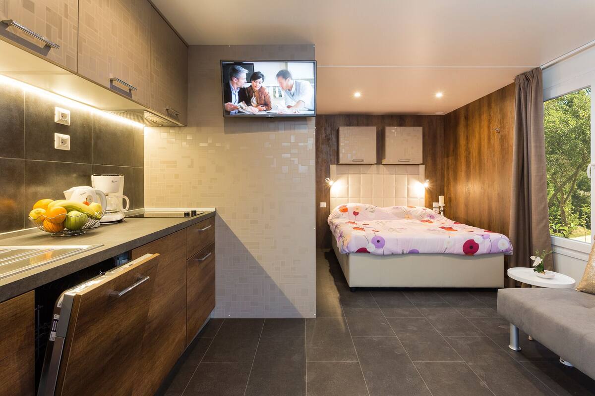 Een moderne hotelkamer met een keukenhoek, een bed met bloemenprint beddengoed en een aan de muur bevestigde televisie.