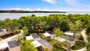 Une rangée de cabanes modernes et écologiques, dotées de panneaux solaires, entourées d’une végétation luxuriante et offrant une vue sur un lac.