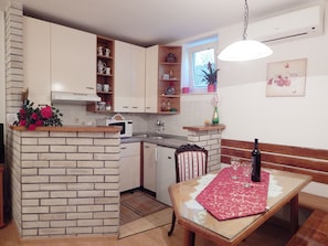A compact kitchen with white cabinets, a microwave, and a sink. There's a dining area with a table set for two, a bench, and a bottle of wine. - Apartments Emi (Split)