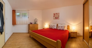 A bedroom with a wooden bed, a nightstand, a dresser, a window with curtains, a wall clock, and a mirror. - Apartments Emi (Split)