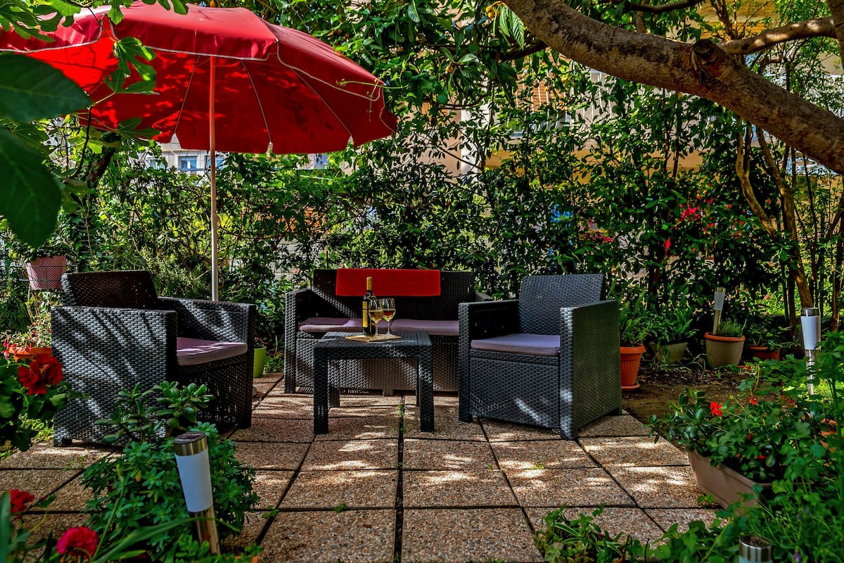 An outdoor patio area with wicker furniture, a red umbrella, and potted plants.