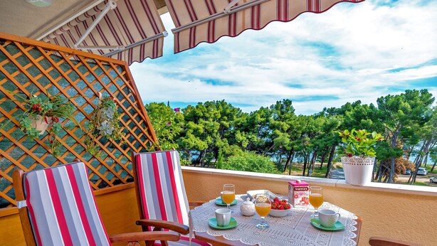 Un balcón con mesa lista para el desayuno, sillas y vistas a árboles y agua.