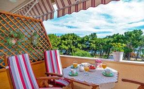 A balcony with a table set for breakfast, chairs, and a view of trees and water. - Apartments Emi (Split)