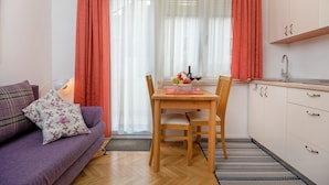 Un espacio habitable funcional con sofá, mesa de comedor con sillas, zona de cocina y ventana con cortinas.