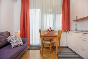 Un ambiente compatto con divano, tavolo da pranzo con sedie, angolo cottura e finestra con tende.