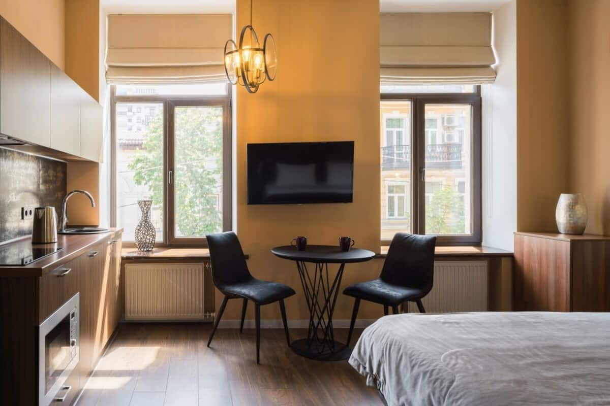 Una habitación de hotel compacta con kitchenette, una cama, un televisor, dos sillas y una mesa.