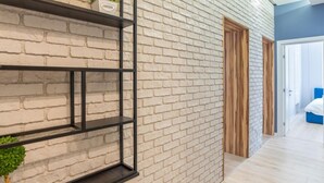 Un couloir avec un mur en briques, une étagère en métal noir ornée de plantes et une porte en bois.