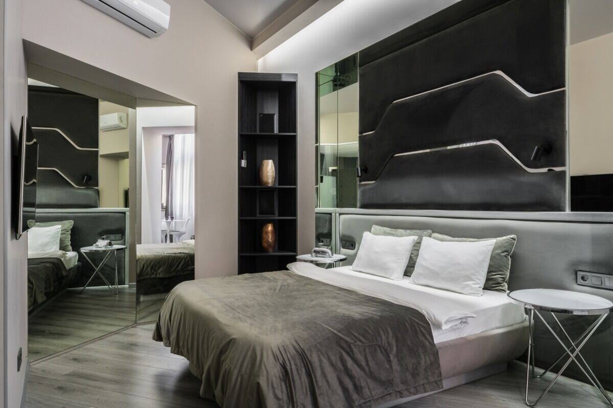 Un dormitorio moderno con una cama grande, una mesita de noche, una estantería empotrada y un espejo.