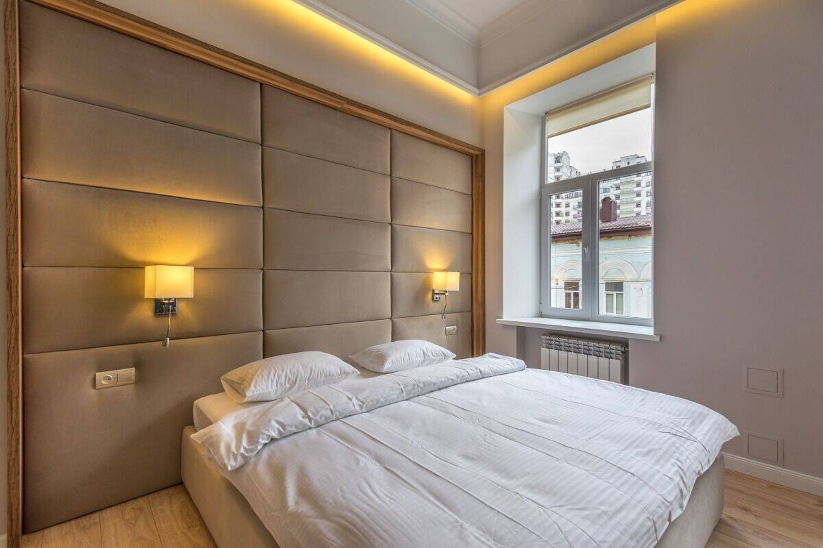 Un dormitorio moderno con una cama grande, dos lámparas de noche y una ventana con vistas a la ciudad.