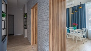 Un intérieur moderne avec un mur en briques, une porte en bois et un coin repas comprenant des chaises blanches et une table.