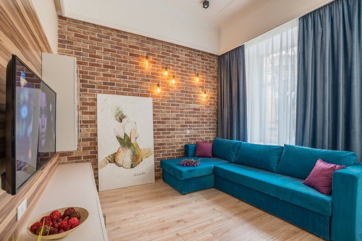 Una sala de estar moderna con una pared de ladrillo, un sofá azul, un televisor de pantalla plana y un cuadro.