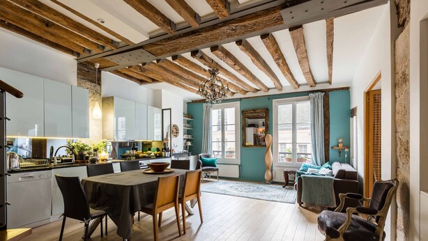Een ruime keuken met moderne apparatuur, een eetgedeelte met houten stoelen, en een gezellige woonkamer met een bank en een open haard.
