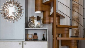 Een spiraaltrap met houten treden en metalen leuningen, een spiegelwand en een kast met decoratieve objecten.