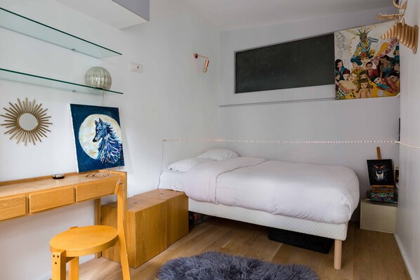 A bedroom with a bed, a desk, a chair, a fluffy rug, and wall art. - Artistic Excellence in the Marais, by Veeve (Paris)