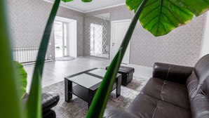 A modern living room with a leather sofa, a glass coffee table, and a patterned rug. There is a large window with a view of the outdoors. - MIxx Hotel (Karakol)