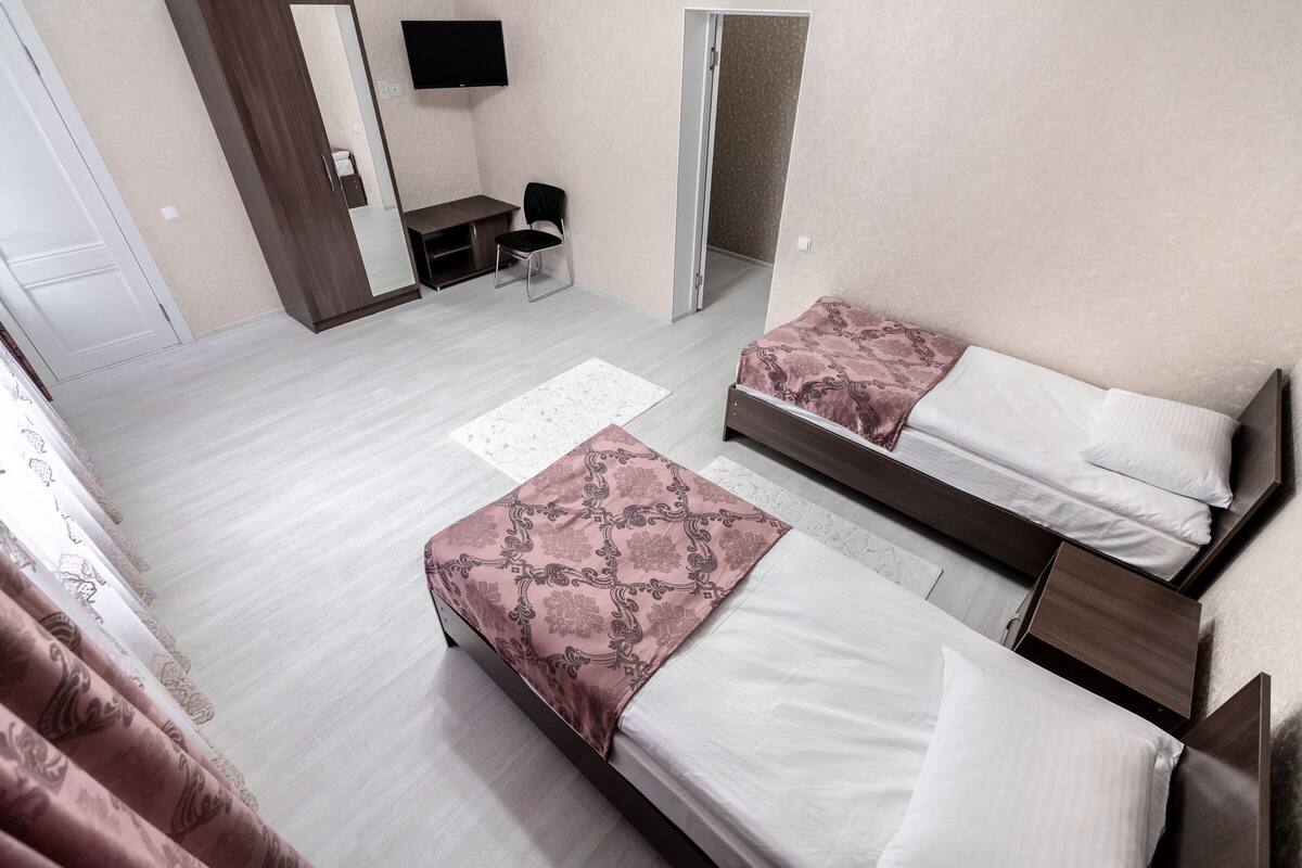 A hotel room with two beds, a desk, a chair, and a TV.