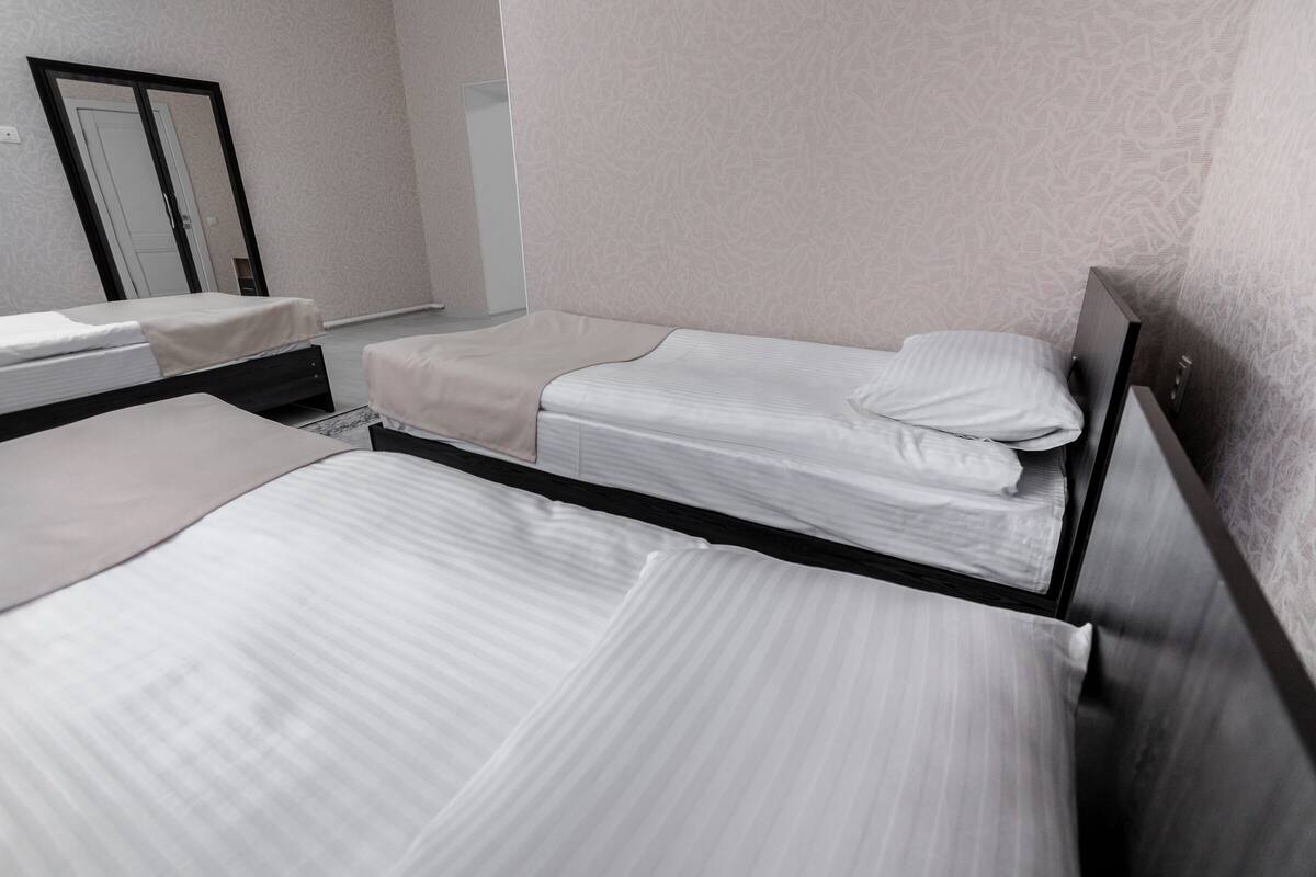A hotel room with three single beds, a wardrobe, and a mirror.