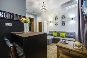 A modern living room with a wooden coffee table, a grey sofa with green cushions, a black leather chair, and a decorative vase with flowers.