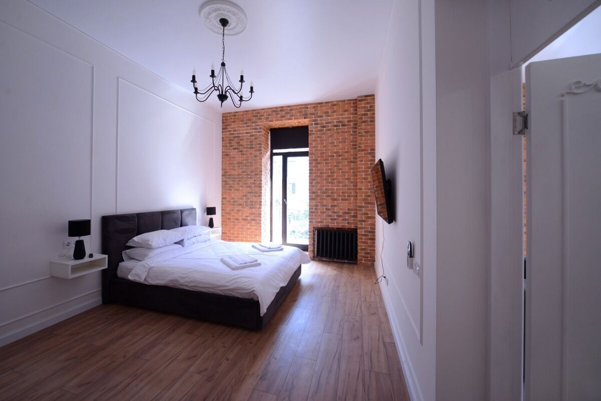 Quarto moderno com parede de tijolos, uma cama, mesa de cabeceira e um lustre.