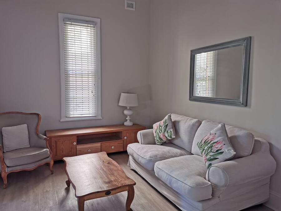 Una sala de estar con una mesa de centro de madera, un sofá con cojines estampados, una mesita auxiliar de madera y un espejo en la pared.
