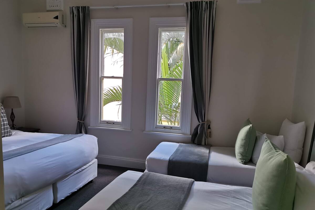 A hotel room with two beds, a nightstand, a lamp, and two windows with curtains.