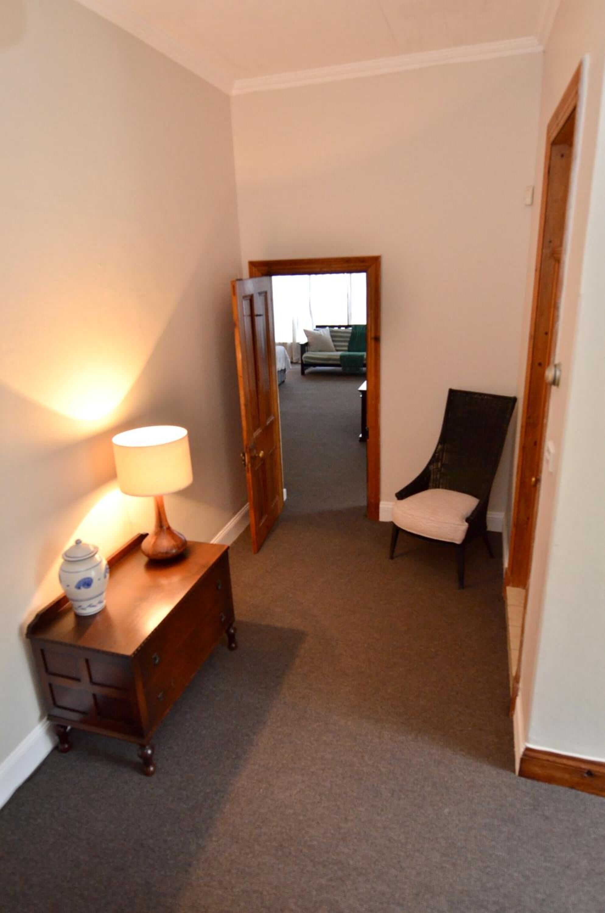 A narrow hallway with a wooden dresser, a lamp, and a chair.