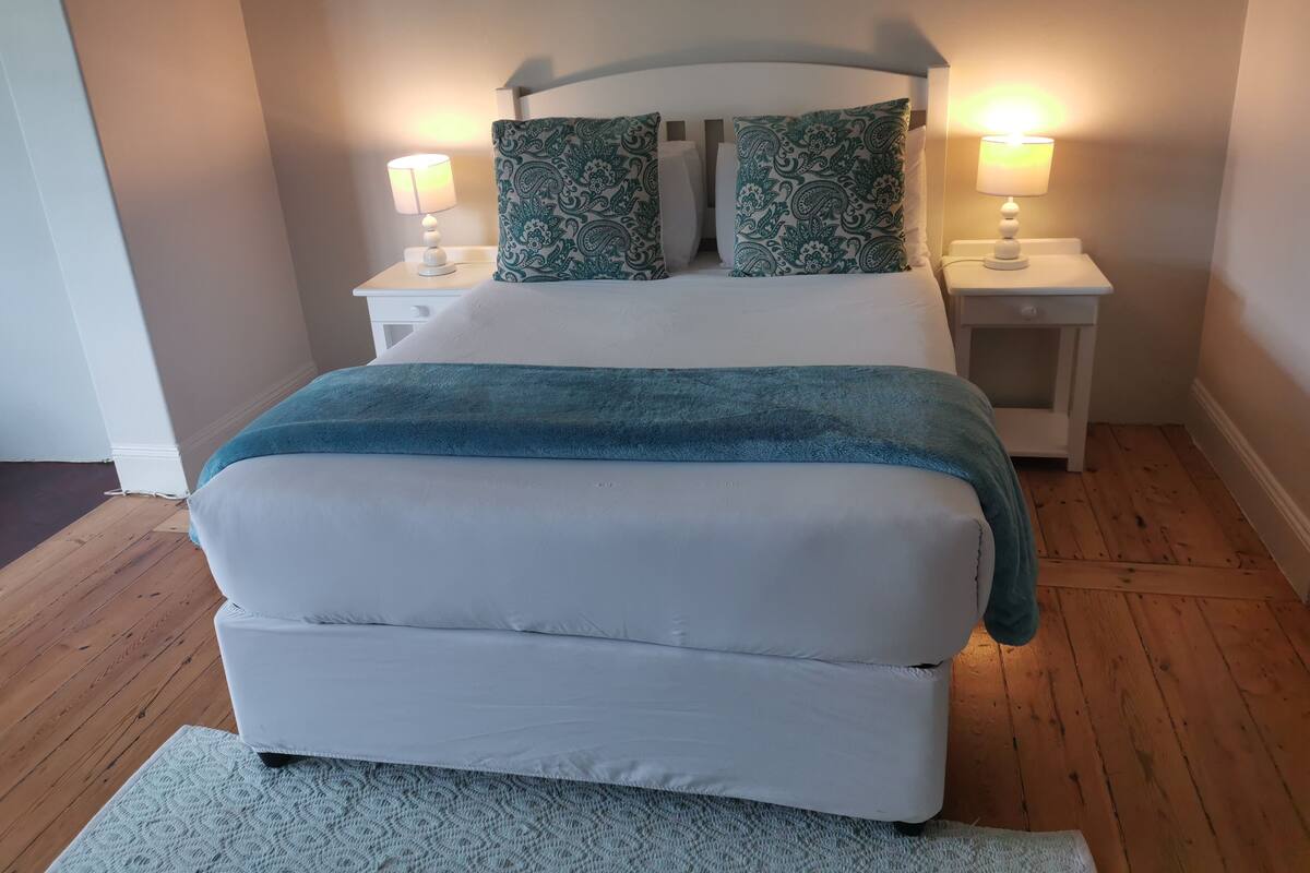 A bed with a white headboard, two matching pillows, and a blue blanket. There are two bedside tables with lamps.