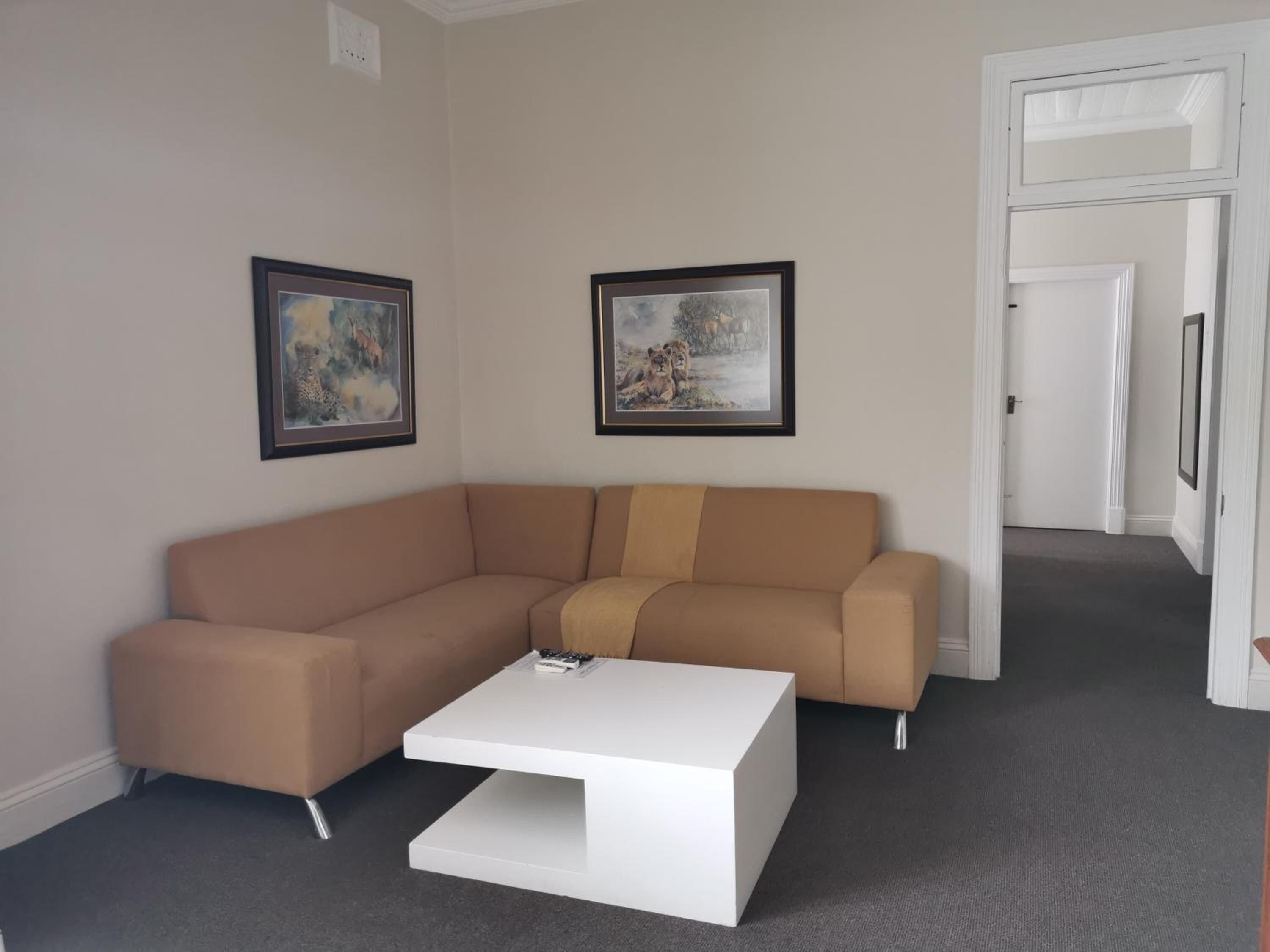 Un salon moderne avec un canapé d’angle beige, une table basse blanche et deux tableaux encadrés accrochés au mur.