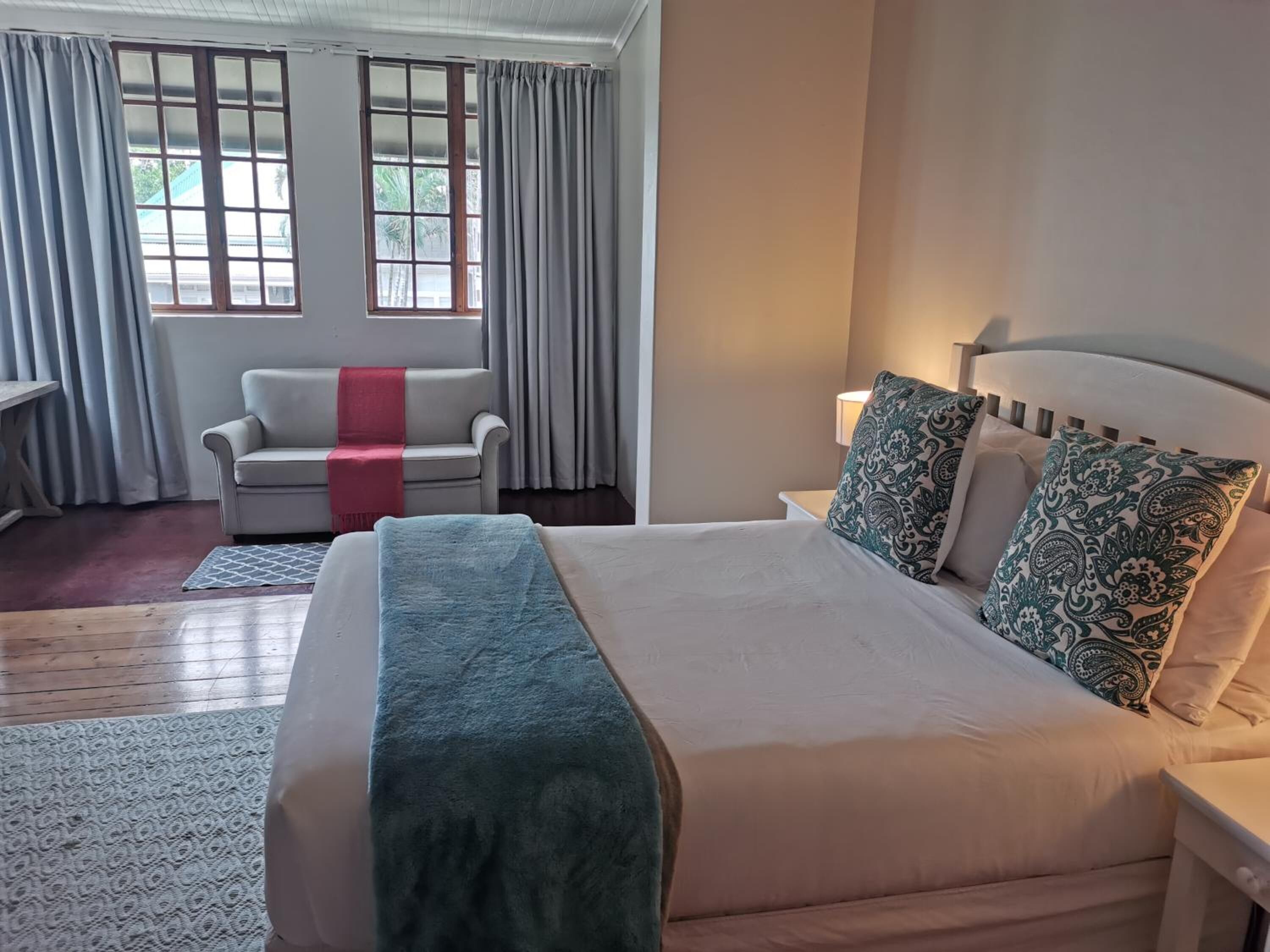 A hotel room with a bed, a sofa, a nightstand, and a window with curtains.