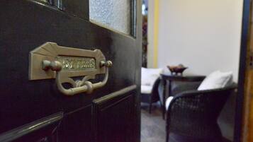 Une porte dotée d’une poignée en laiton et d’une plaque nominative, une chaise noire et une petite table surmontée d’un coussin blanc.