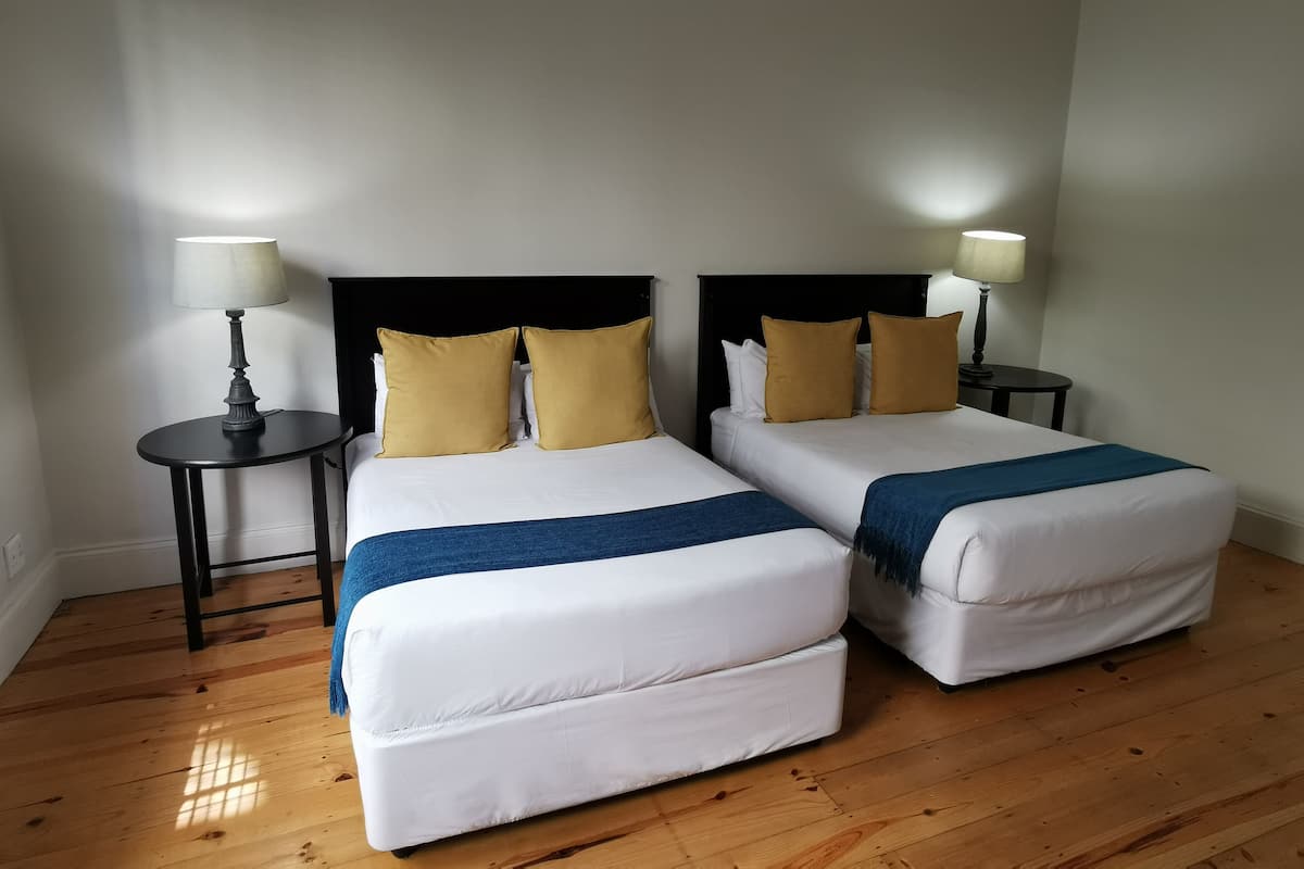 A hotel room with two beds, each with white bedding and blue throw blankets, and two bedside tables with lamps.