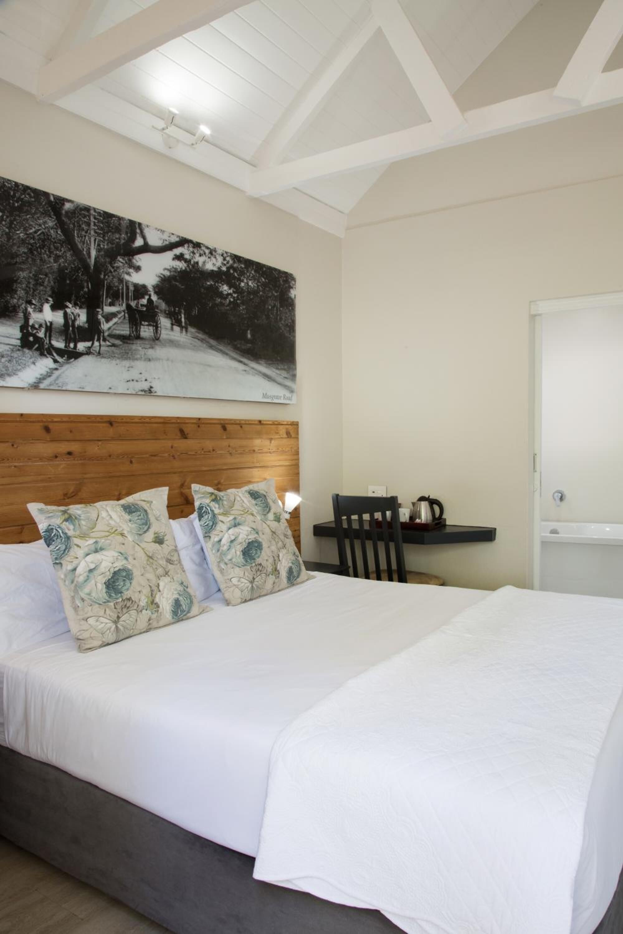 Ein Schlafzimmer mit Bett, Holz-Kopfteil, einem Wandbild, einem kleinen Tisch mit Wasserkocher und einer Tür.