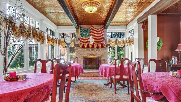 Un comedor con manteles rojos, sillas de madera y una alfombra estampada.