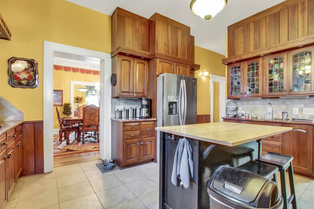 A kitchen with wooden cabinets, a stainless steel refrigerator, a dining table with chairs, and a small island with a sink.