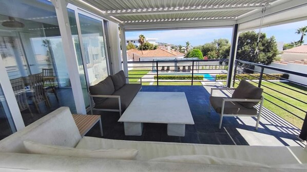 A covered outdoor seating area with a sofa, chairs, and a table. - Detached villa private pool and sea views (Sotogrande)