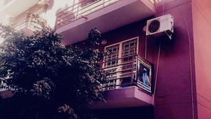 Un immeuble à plusieurs étages doté de balcons, de climatiseurs et d’un arbre devant.