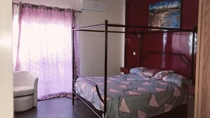 Une chambre à coucher avec un lit à baldaquin, une chaise, un tableau accroché au mur et une fenêtre avec des rideaux.