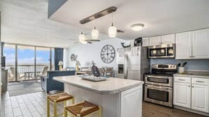 Una cocina moderna con armarios blancos, una isla central con taburetes y electrodomésticos de acero inoxidable, además de un amplio ventanal con vistas.