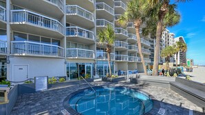 Un hotel con una piscina circular rodeada por un patio de ladrillo, palmeras y vistas a la playa.
