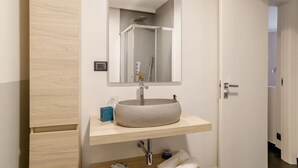 A bathroom with a round vessel sink, a mirror above it, and a door leading to another room. - Ravecca Luxury apartment in the heart of the centre - 2 bedrooms (GENOVA)