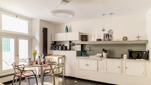 A modern kitchen with white cabinetry, a dining area with a round table and chairs, and a large window providing natural light. - Ravecca Luxury apartment in the heart of the centre - 2 bedrooms (GENOVA)