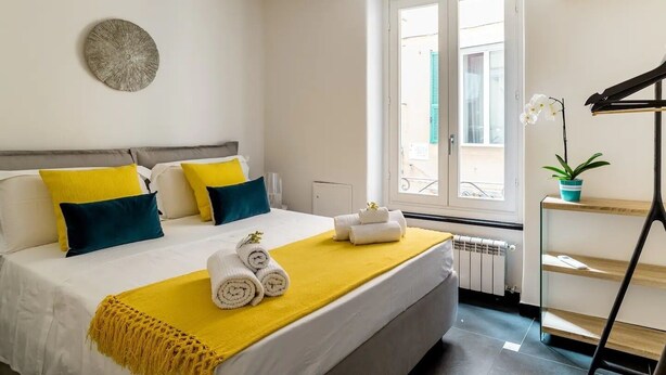 A neatly arranged hotel room with a bed, pillows, a yellow throw, and a potted plant. - Ravecca Luxury apartment in the heart of the centre - 2 bedrooms (GENOVA)