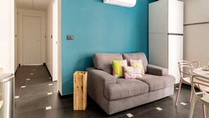 A modern living room with a teal accent wall, grey sofa, and a small dining area with pink chairs. - Ravecca Luxury apartment in the heart of the centre - 2 bedrooms (GENOVA)